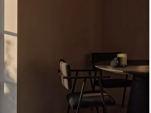 A candle in smoked glass on a dark table in warm evening light